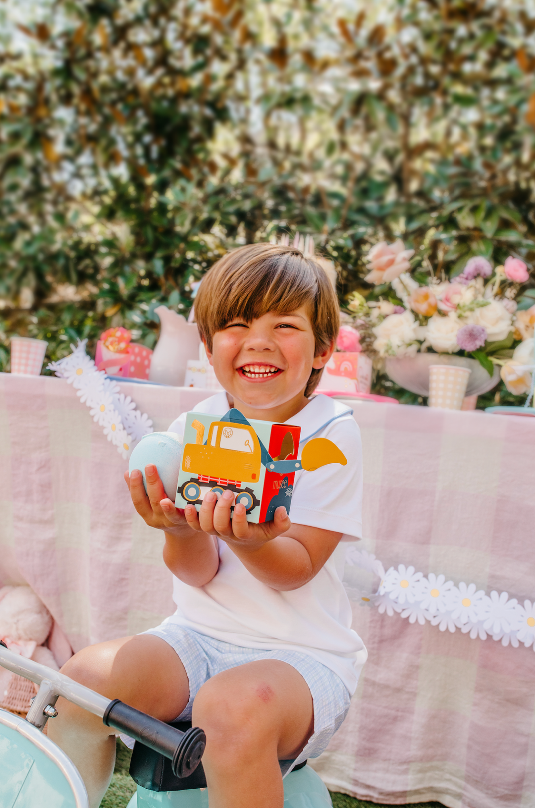 Smiling boy holding the excavator box and a blue bath bomb at a garden construction birthday party