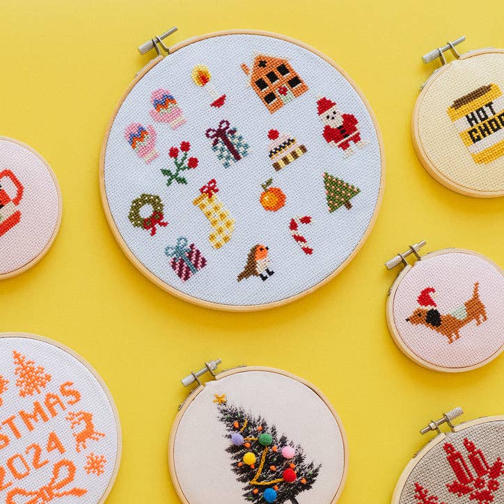 Christmas sampler hoop among festive Cotton Clara cross stitch designs on yellow