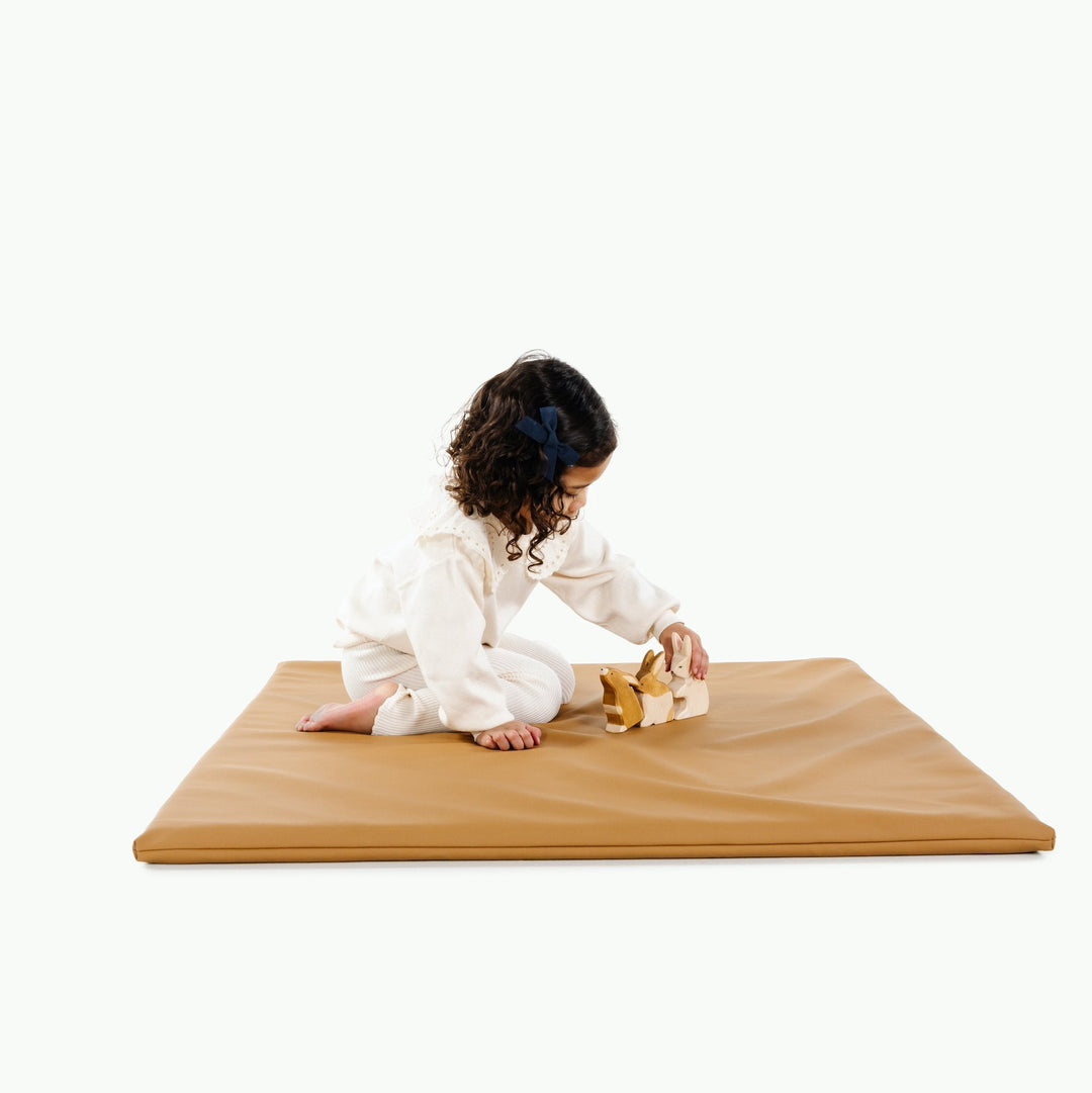 Girl sitting on the square camel vegan leather padded play mat with wooden animal toys