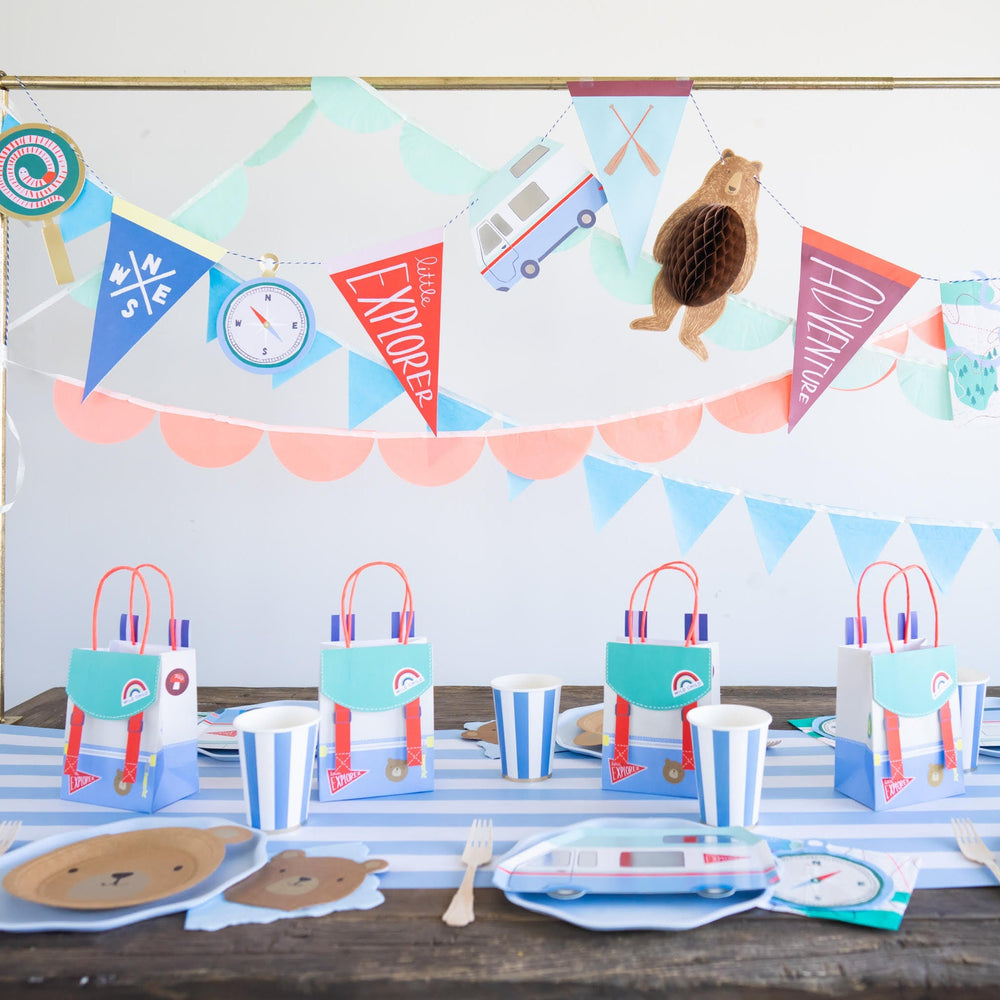 Camping adventure backpack bags at a full camping party setup with plates, napkins, and garland