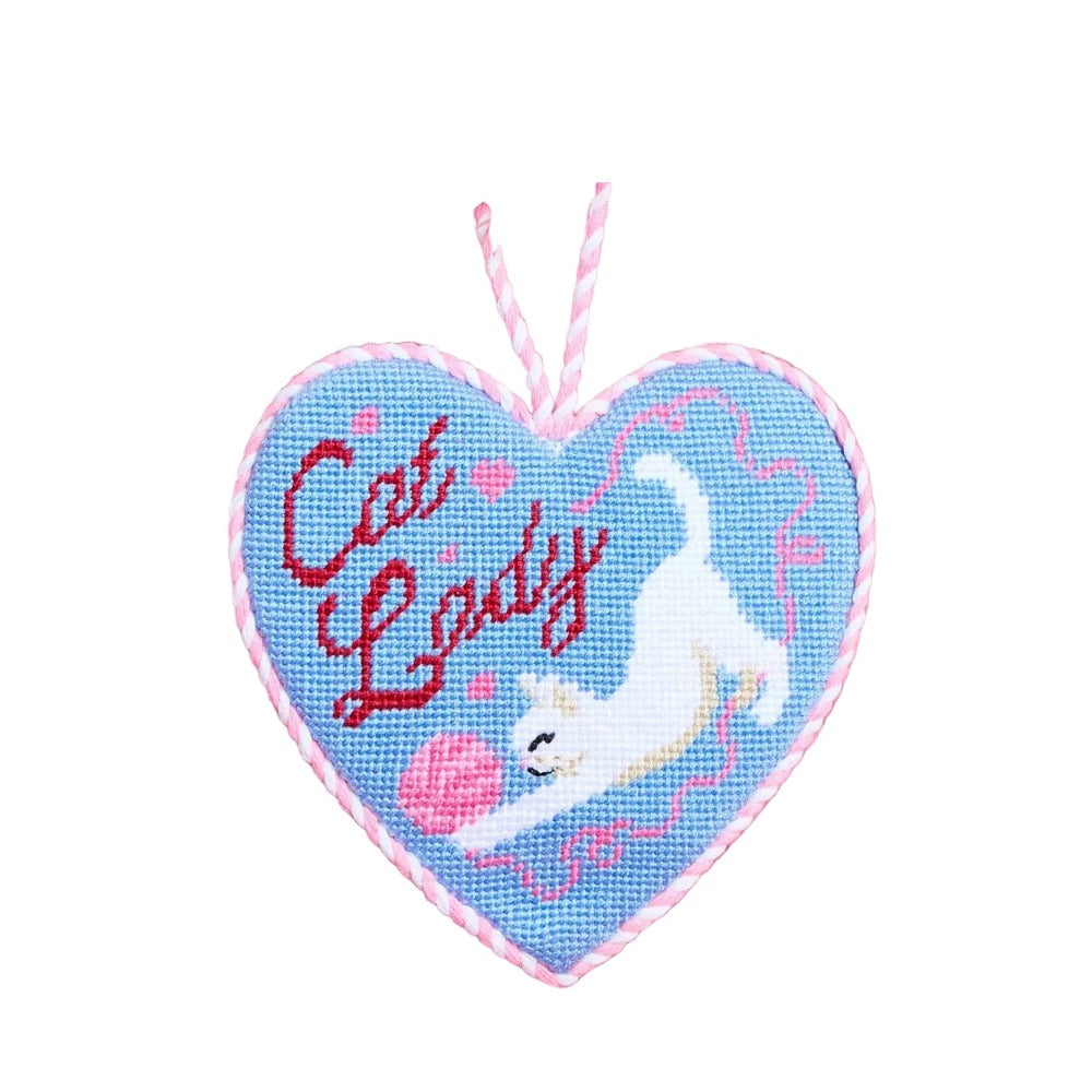 Blue heart needlepoint ornament stitched with red Cat Lady script, a white cat, and pink yarn, with a pink cord