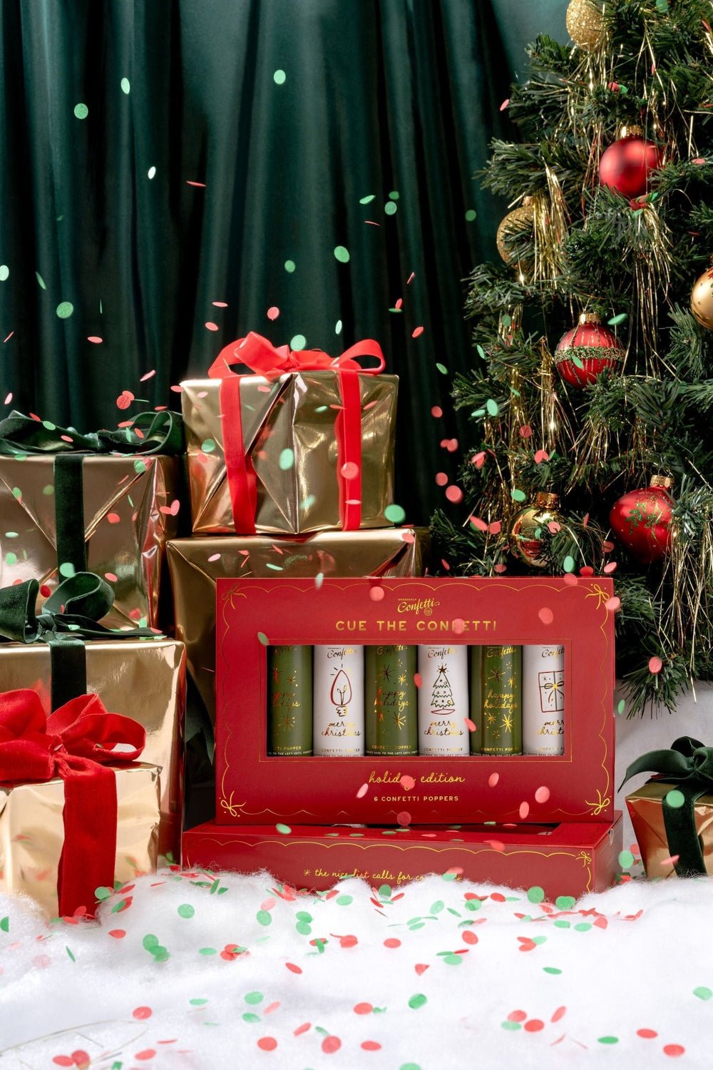 Red and gold Christmas confetti popper box beside wrapped gifts under a decorated tree