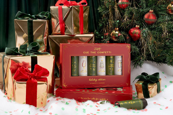 Red Christmas confetti popper box propped against gold and red wrapped presents by the tree