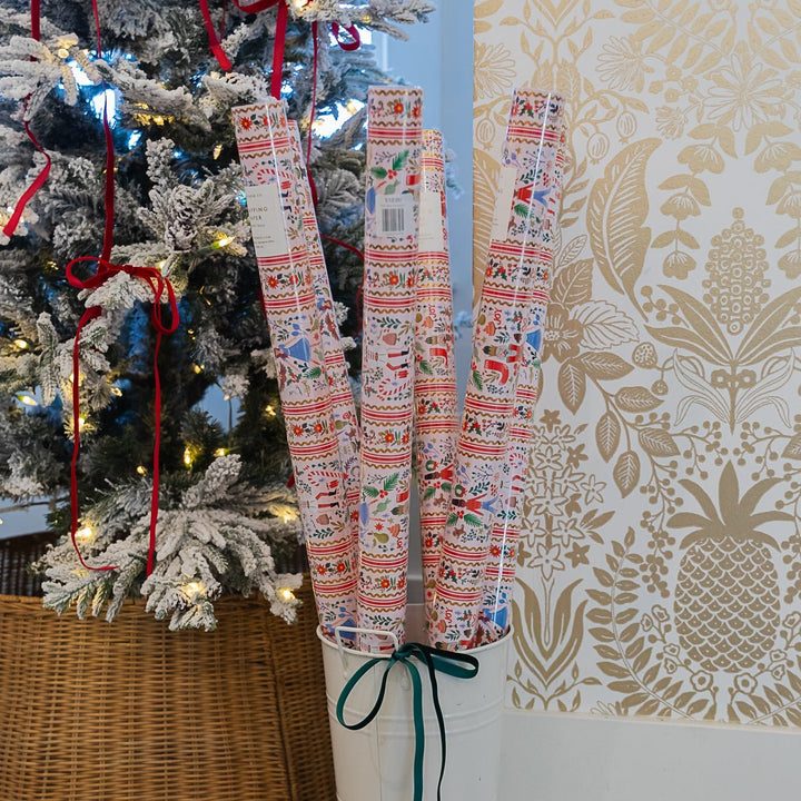 Rolls of Holly Jolly Nutcracker Christmas wrapping paper in a bucket beside a flocked tree
