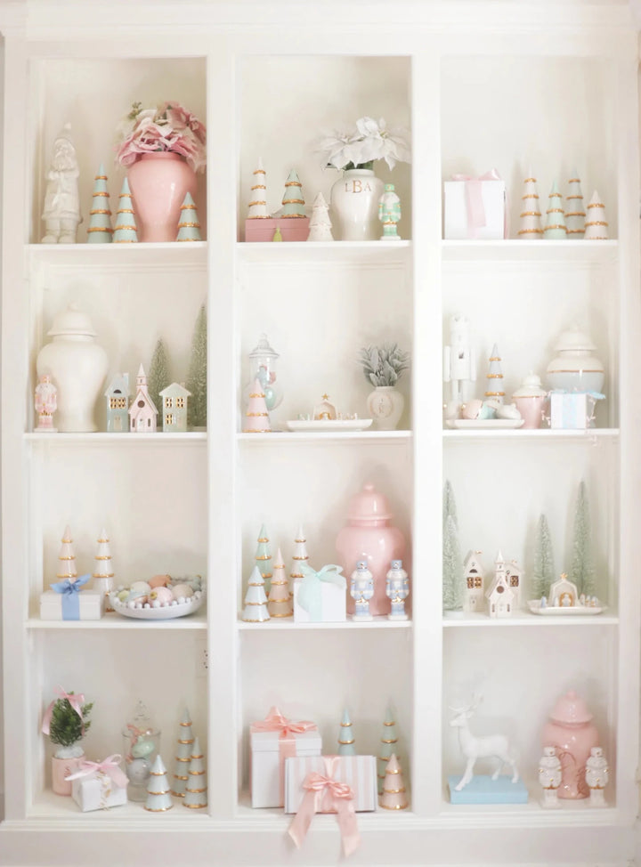 Tall white cubby shelves filled with ivory houses, bottle brush trees, and pastel Christmas decor
