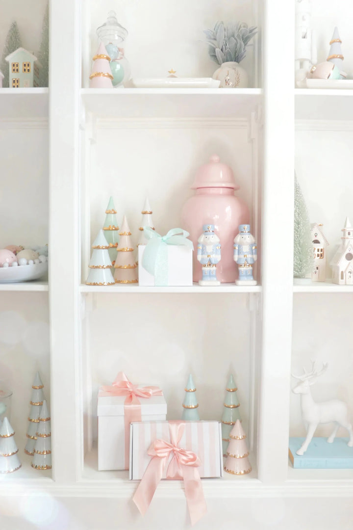 White bookcase styled with ivory ceramic village houses, pastel ginger jars, and pink wrapped gifts for the holidays