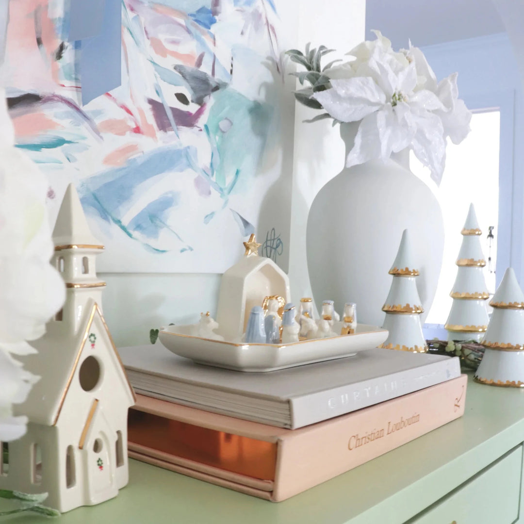 Ivory ceramic church and houses on a stack of books beside a white vase of poinsettias for pastel Christmas decor