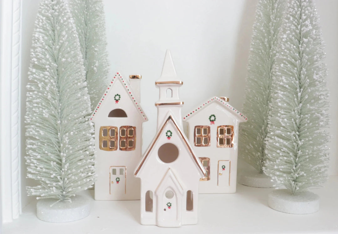 Ivory ceramic church and houses with gold trim between frosted sage bottle brush trees for Christmas mantel decor