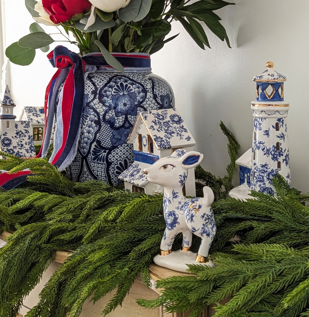 Decorative scene with a blue and white ceramic deer, gingerbread houses, and a floral arrangement.