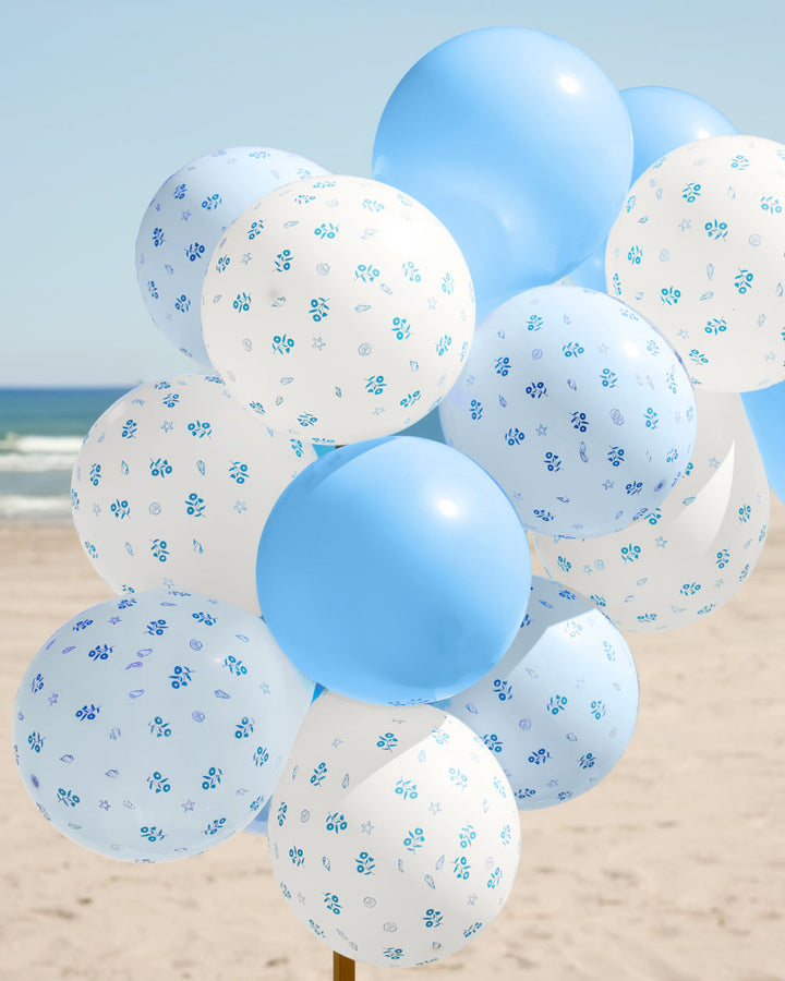 Bunch of coastal blue and white latex balloons with a blue floral print on a beach backdrop