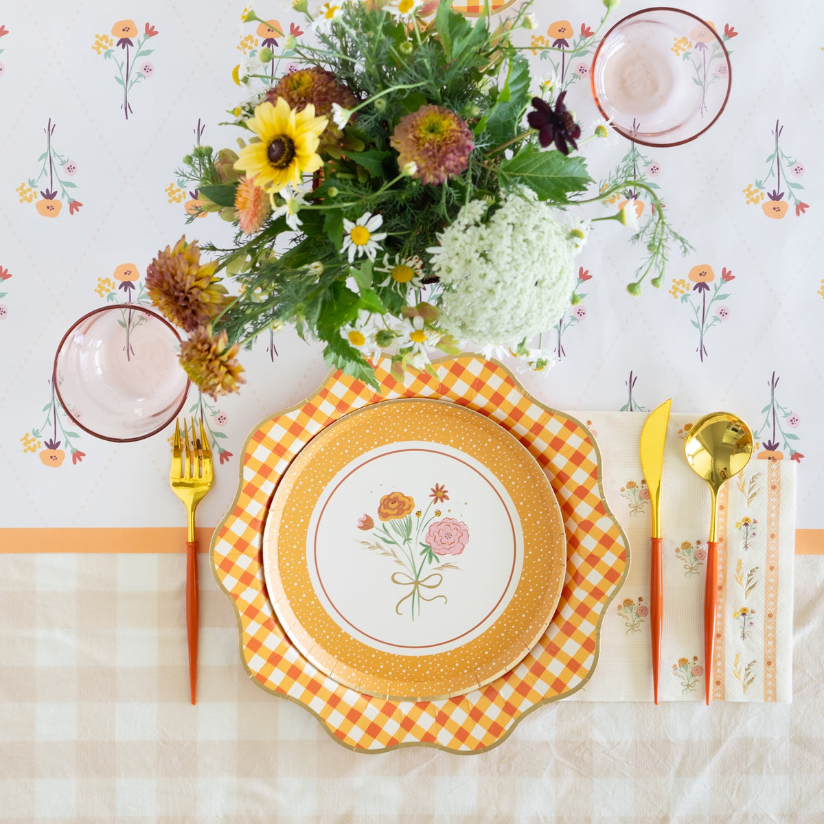 A styled Thanksgiving table setting with gingham party supplies and a fall floral arrangement.