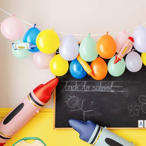 Crayon balloons with a pastel balloon garland over a back to school chalkboard