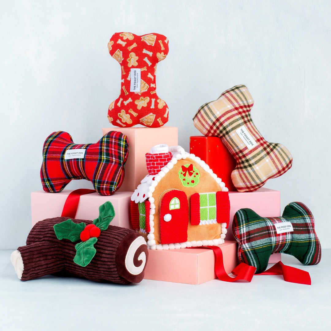 Plaid bone toys, gingerbread house, and yule log stacked on pink blocks against pale blue