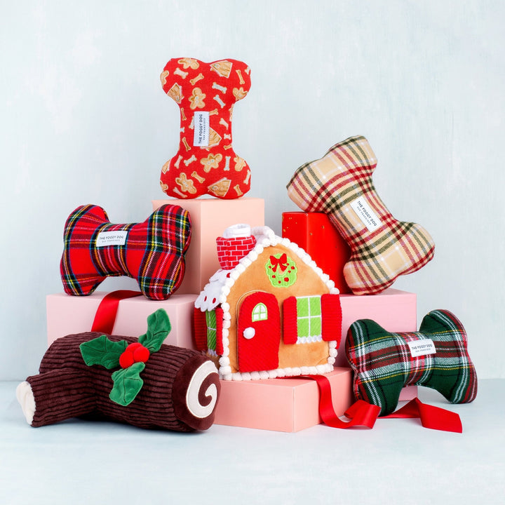 Plaid bone toys, a gingerbread house, and the yule log stacked on pink blocks against pale blue