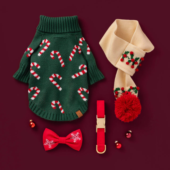 Flat lay on burgundy: candy cane sweater, cream candy cane scarf, and a red bow tie