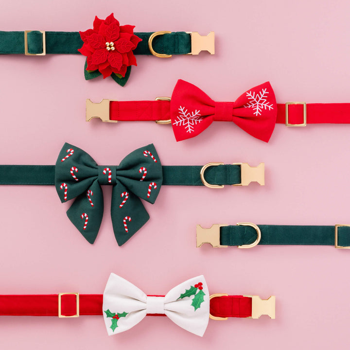 Pink flat lay of holiday collars with a poinsettia, red bow tie, and green candy cane bow