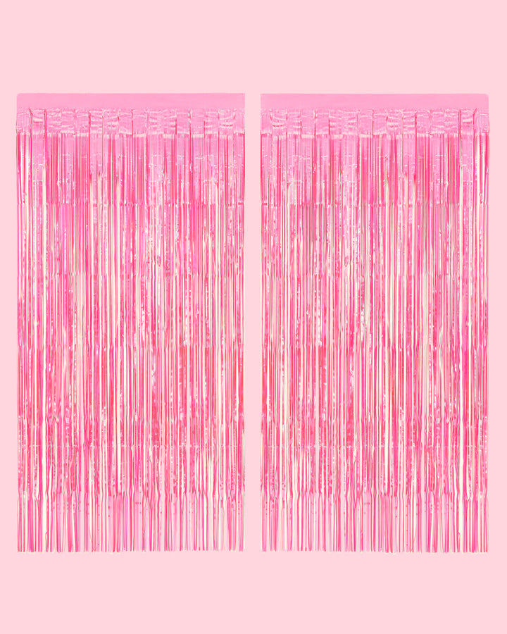 Two hot pink iridescent fringe curtain panels hung side by side on a pale pink wall