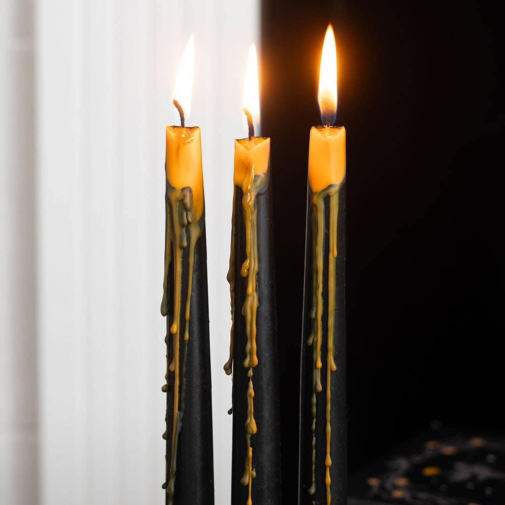 Three lit black tapers oozing orange wax down their sides, a glowing centerpiece for a spooky dinner table