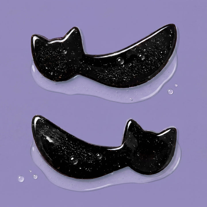 Two glitter flecked black cat eye patches glistening on a purple backdrop, whisker shaped Halloween depuffing