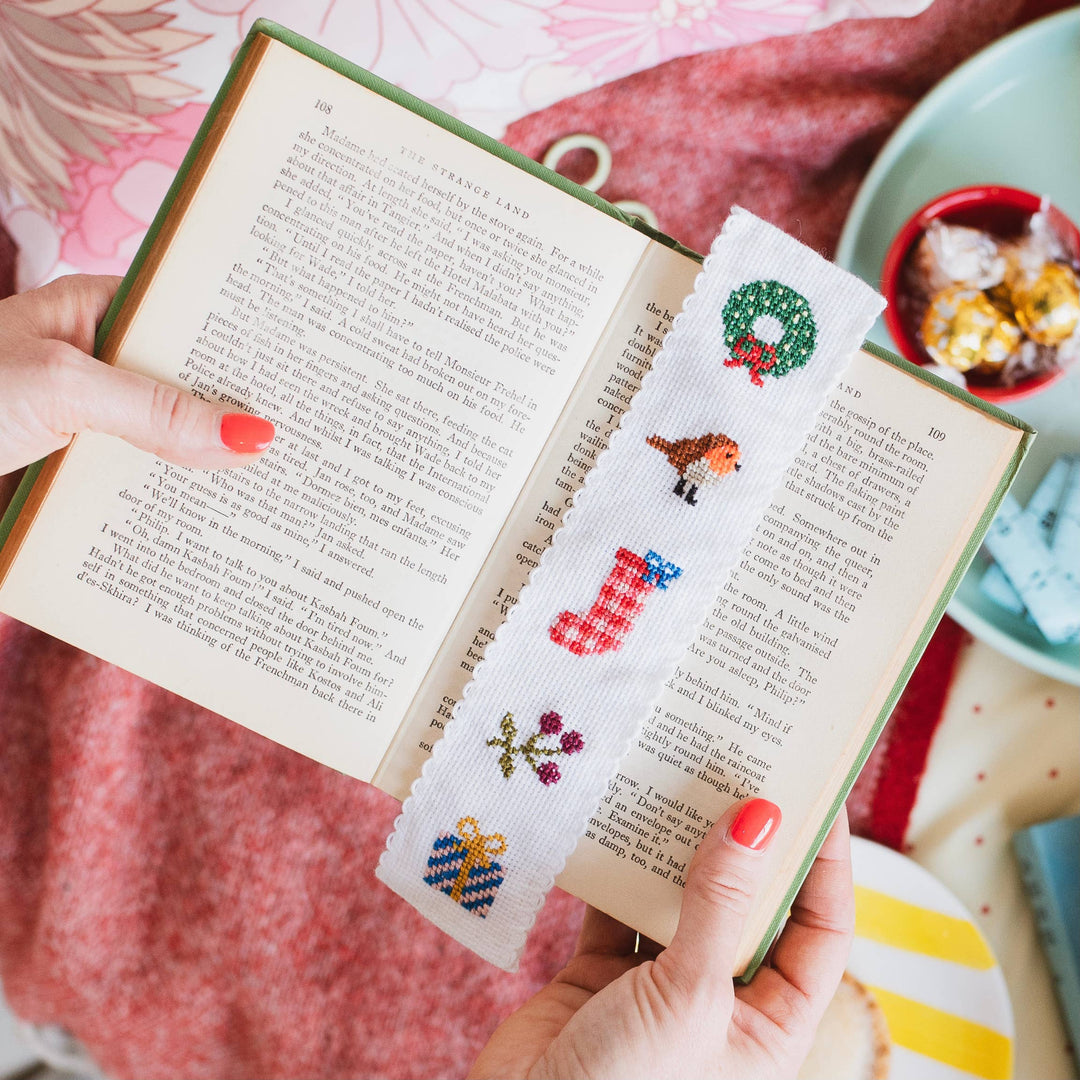 Christmas cross stitch bookmark resting in an open book with chocolates nearby