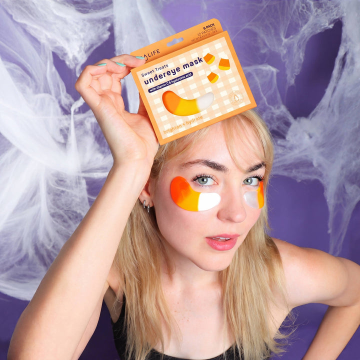 Model wearing candy corn eye patches holding the box overhead against cobwebs, Halloween party prep