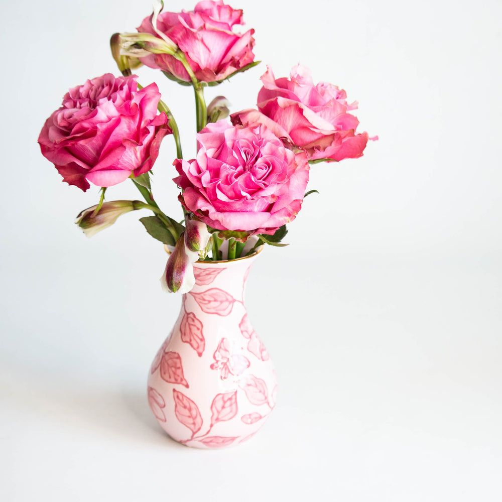 Pink blossom chinoiserie vase holding a bouquet of magenta garden roses against a white backdrop