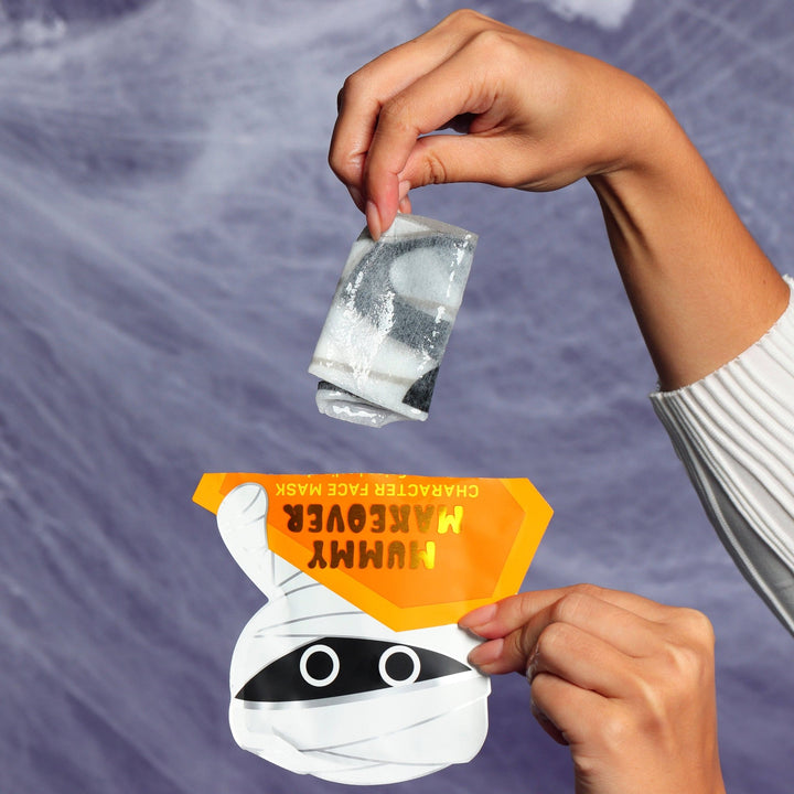 Hands unfolding the rolled mummy sheet mask above its pouch with a webby background, Halloween party prep
