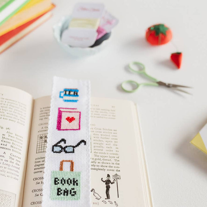 Bookish cross stitch bookmark in a book beside mint embroidery scissors