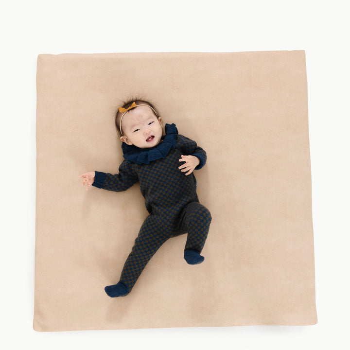 Sand suede square padded play mat, overhead view with a baby lying on it.