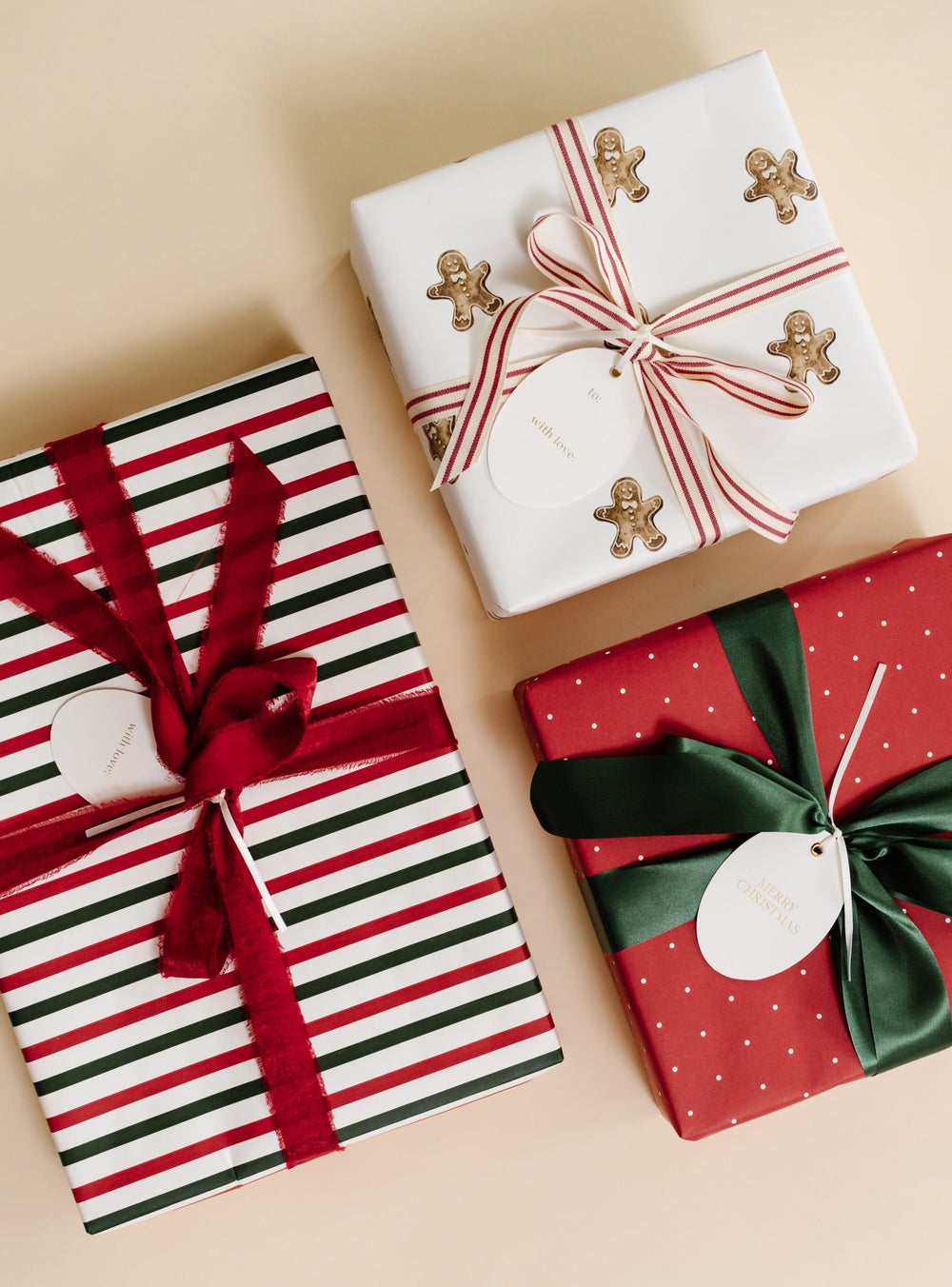 Three gifts in gingerbread print, red polka dot, and red and green stripe paper with ribbon bows on cream