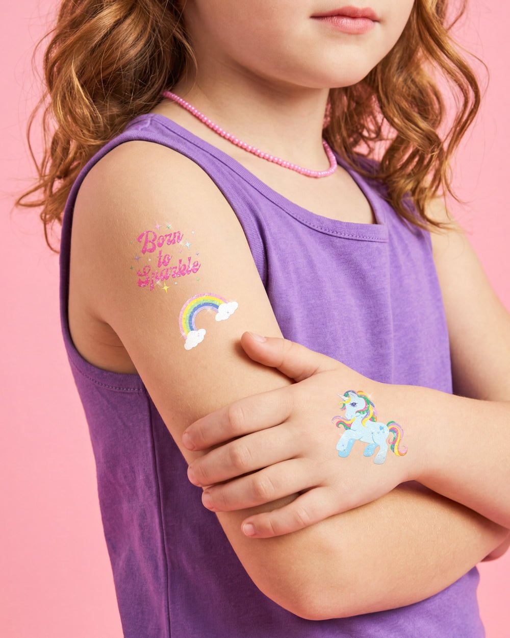 Girl in a purple tank top wearing Born to Sparkle and rainbow tattoos on her shoulder at a kids party