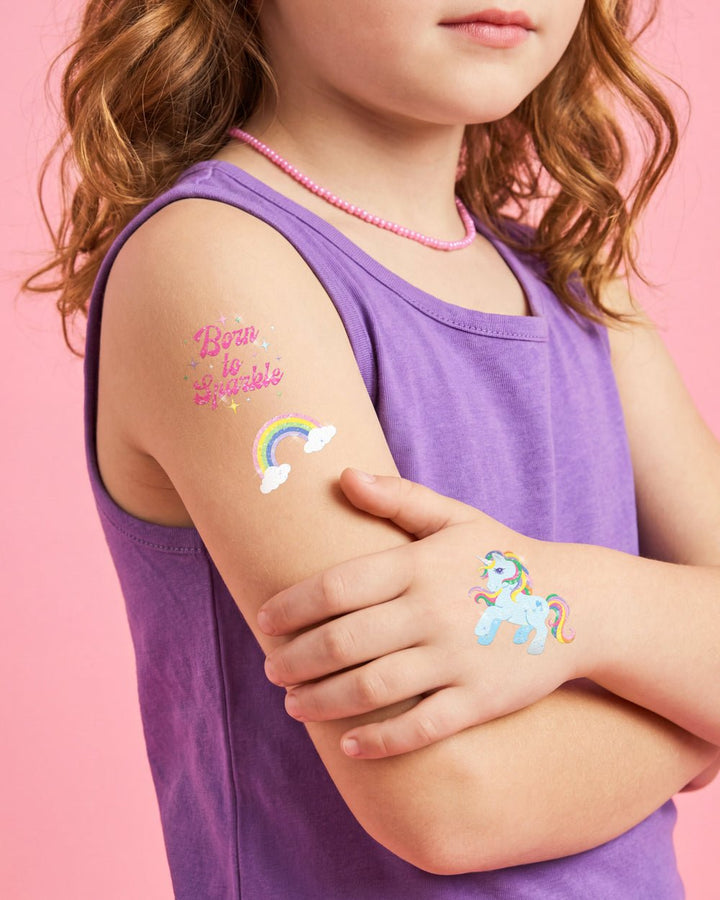 Girl in a purple tank top wearing Born to Sparkle and rainbow tattoos on her shoulder at a kids party