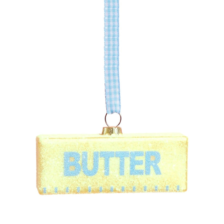 Front view of the yellow glitter glass butter stick ornament with blue BUTTER lettering and a blue gingham ribbon on white