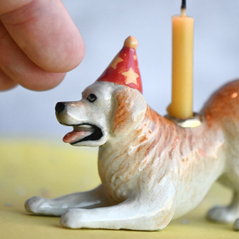 Golden retriever cake topper shown next to a fingertip for scale, a small porcelain dog holding a birthday candle