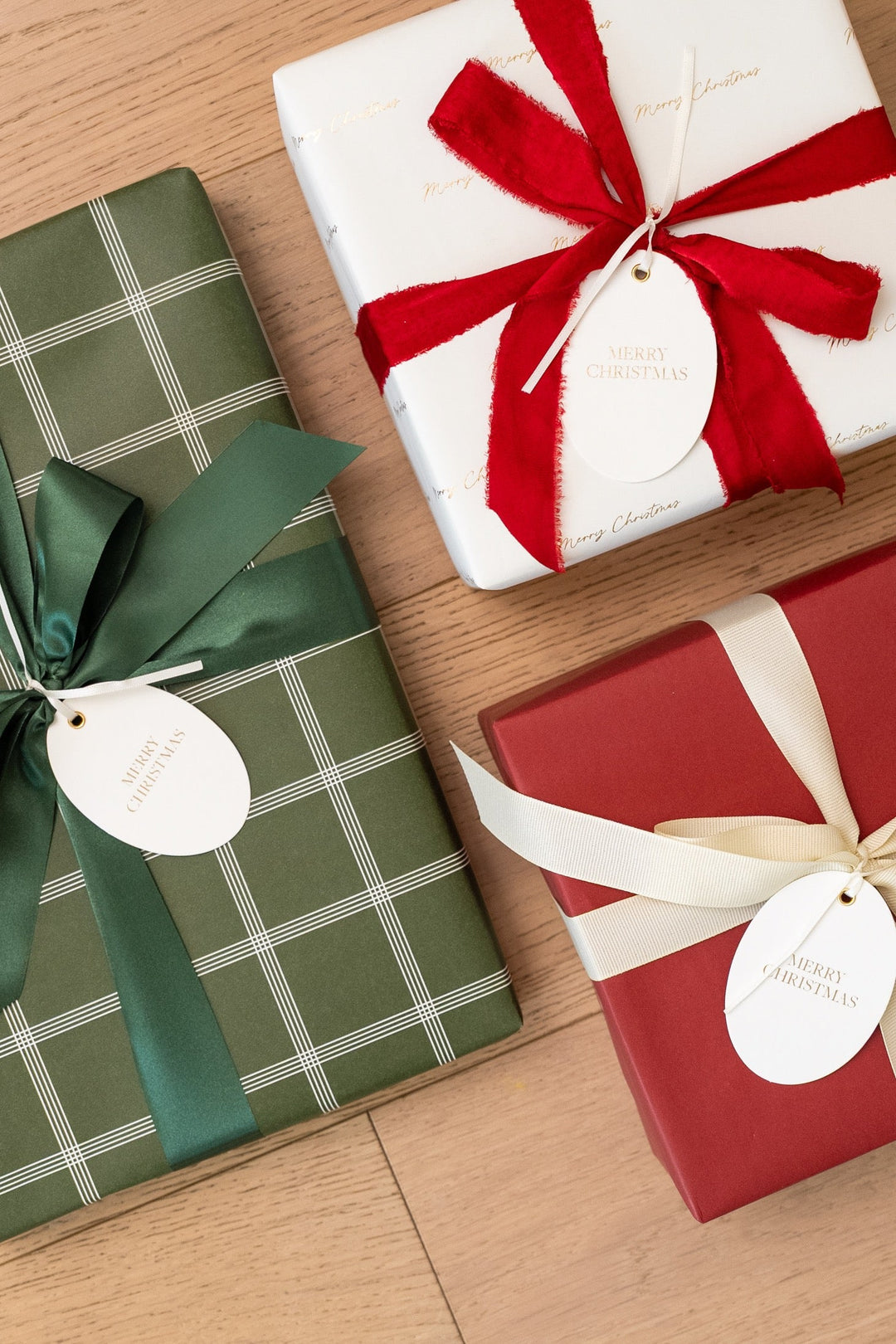 Gifts in white gold script, green windowpane plaid, and solid red paper with ribbon bows on wood