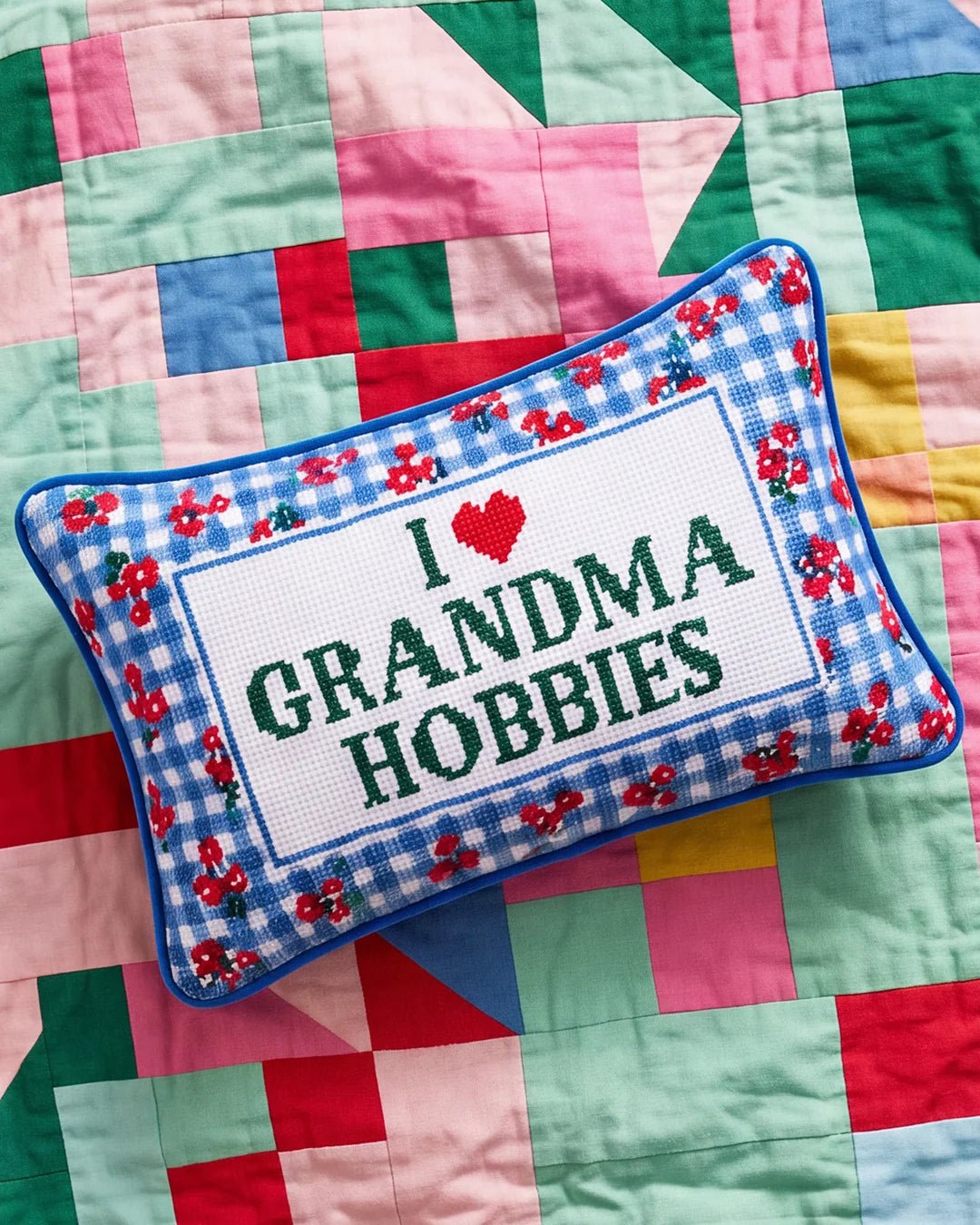 Grandma Hobbies needlepoint pillow lying on a pink, green, and blue patchwork quilt