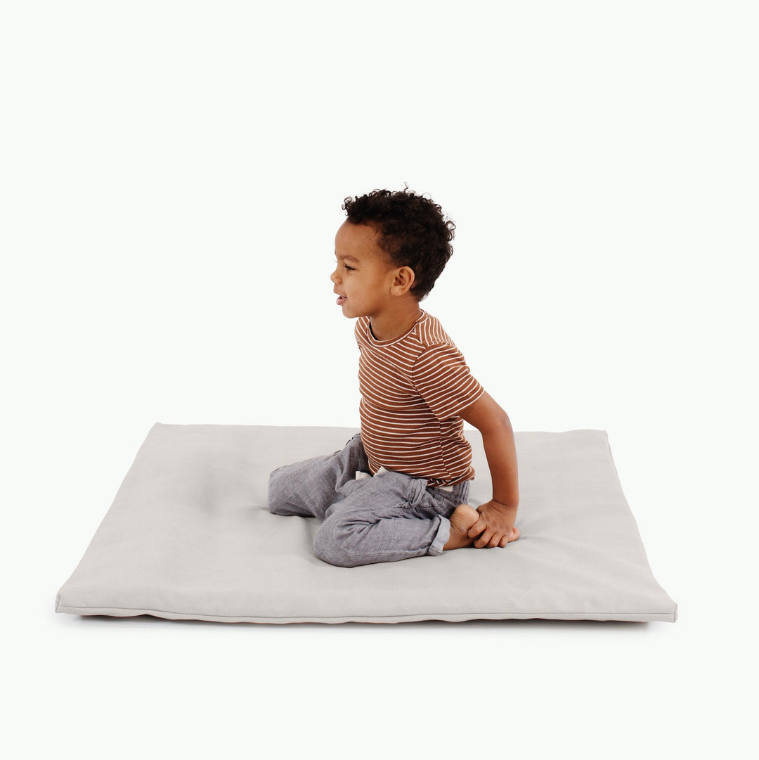 Light grey padded baby play mat with a kneeling toddler in a striped shirt.