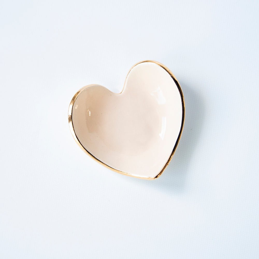Pale peach heart ring dish with a gold rim, angled view on white