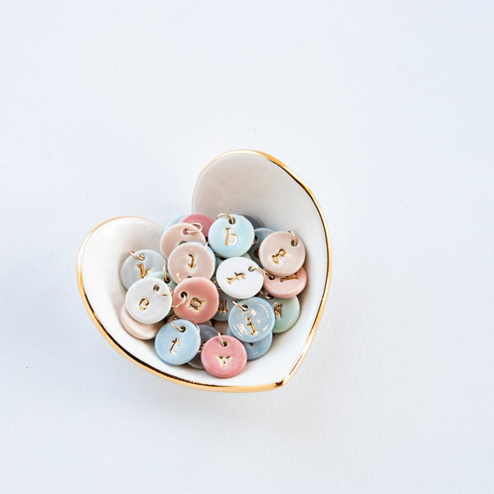 White heart dish with a gold rim holding small round pastel charms