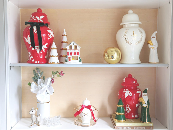 Decorative shelf with Christmas-themed vases, figurines, and ornaments against a beige wall.
