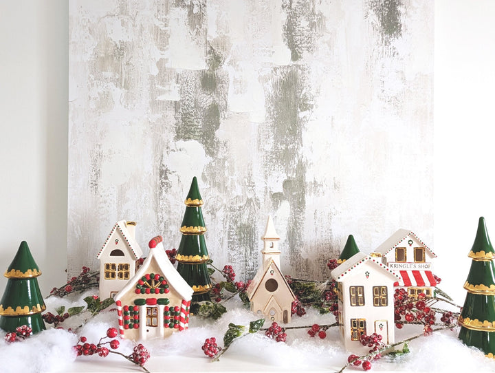 Ceramic Christmas village styled on faux snow with green ceramic trees and red berry garland for holiday mantel decor