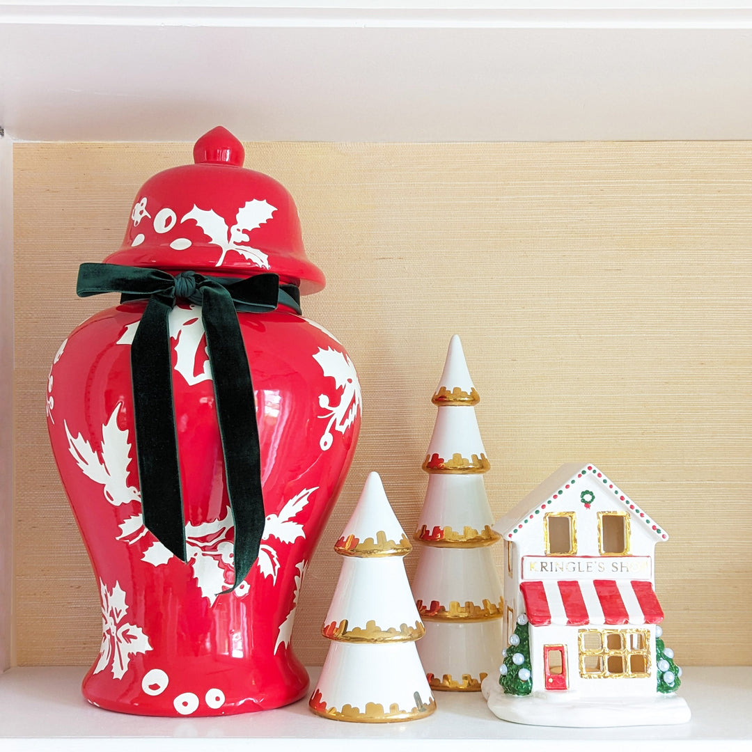 Decorative red vase with white floral patterns, black ribbon, and small Christmas-themed house and trees on a light wooden background.