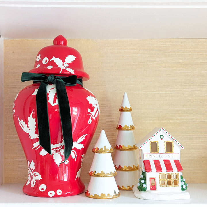 Decorative red vase with white floral patterns, black ribbon, and small Christmas-themed house and trees on a light wooden background.