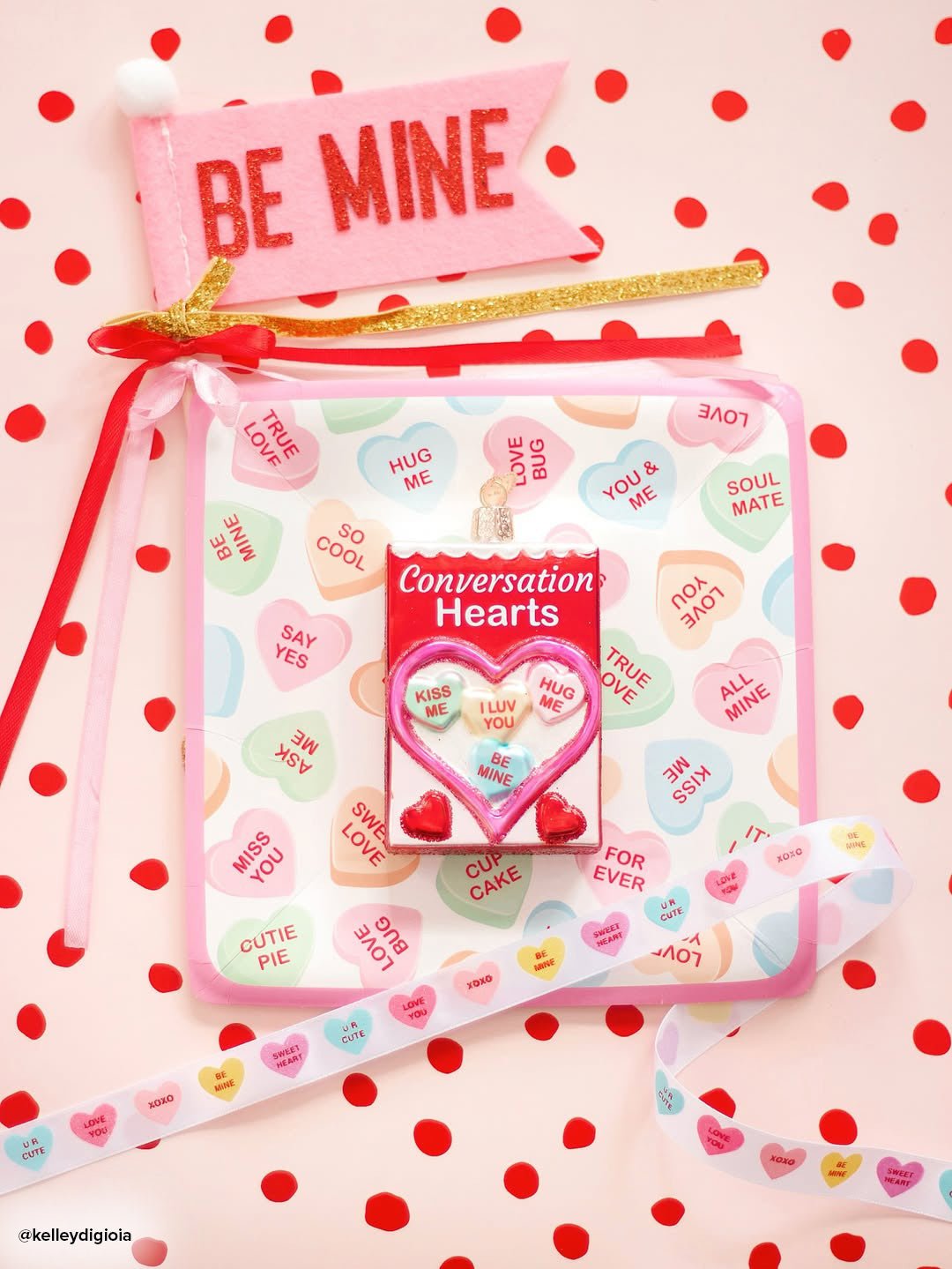Conversation hearts ornament styled on a pink polka dot surface with a Be Mine pillow and ribbon