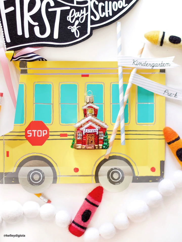 Schoolhouse ornament on a yellow school bus plate with crayons and a first day of school pennant