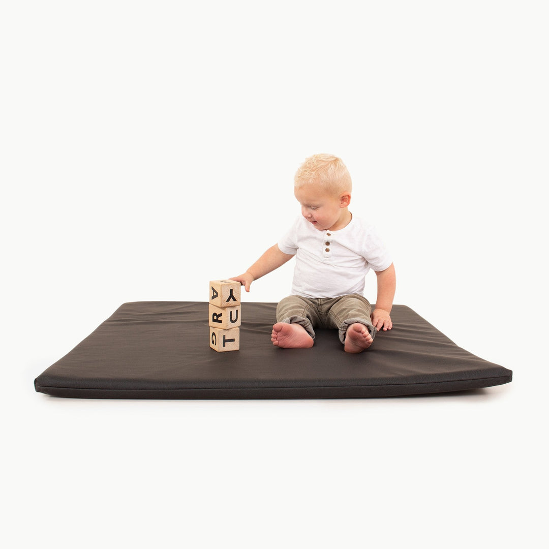 Boy sitting on the square black vegan leather padded play mat stacking wooden alphabet blocks
