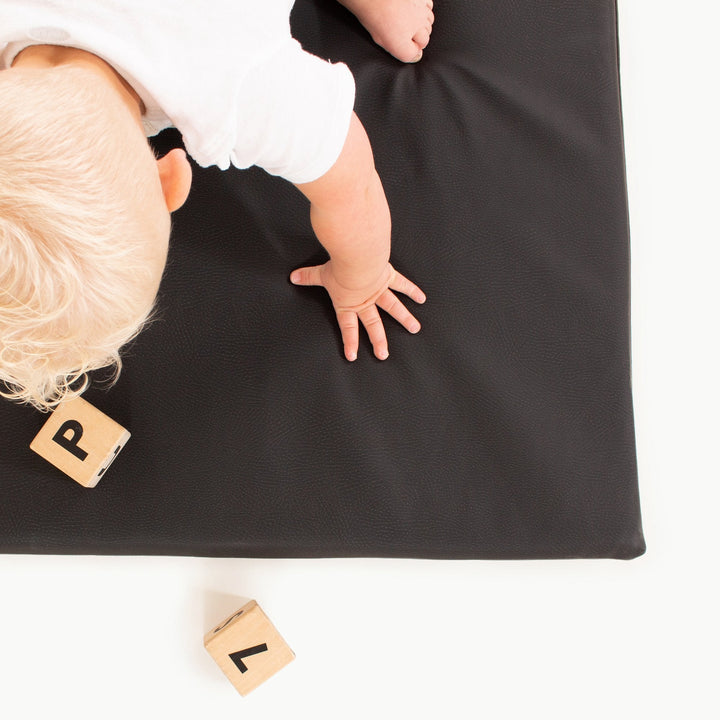 Overhead view of a baby crawling on the black vegan leather padded play mat with wooden alphabet blocks