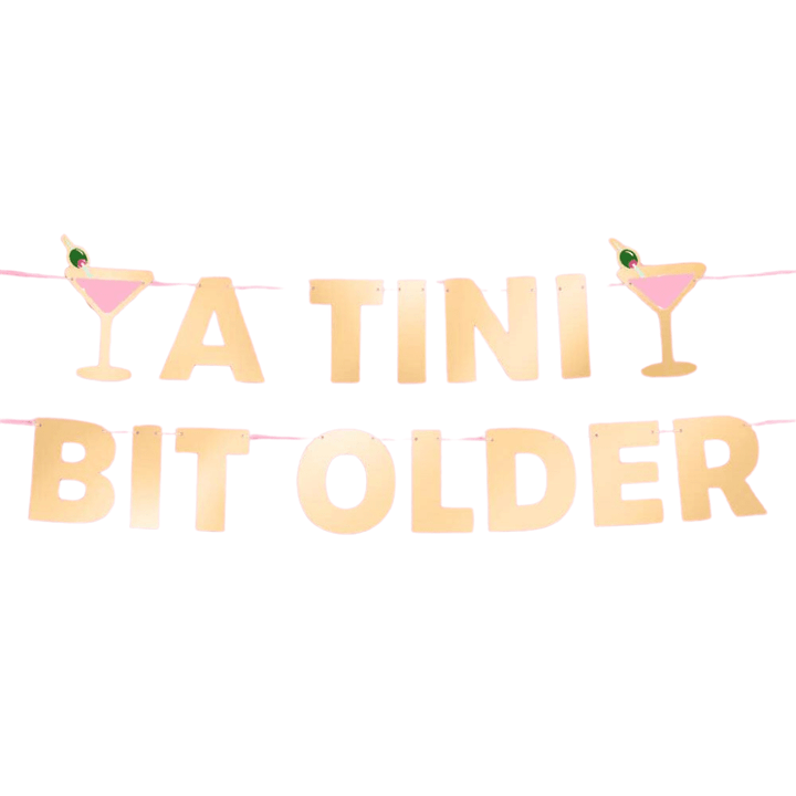 A Tini Bit Older gold foil birthday banner on white, two pre-strung lines with pink martini glass and olive accents