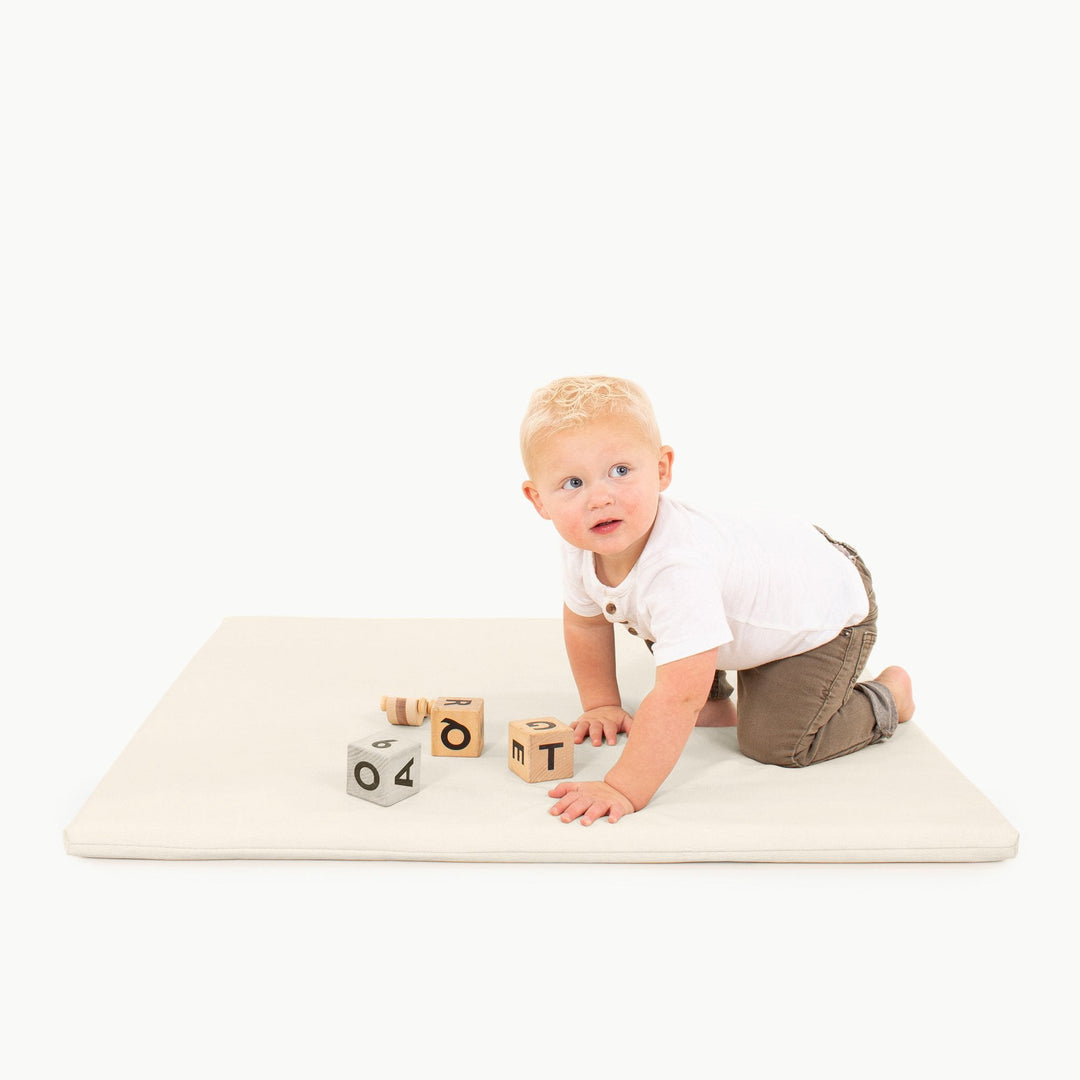 Toddler crawling on the square ivory vegan leather padded play mat with wooden alphabet blocks