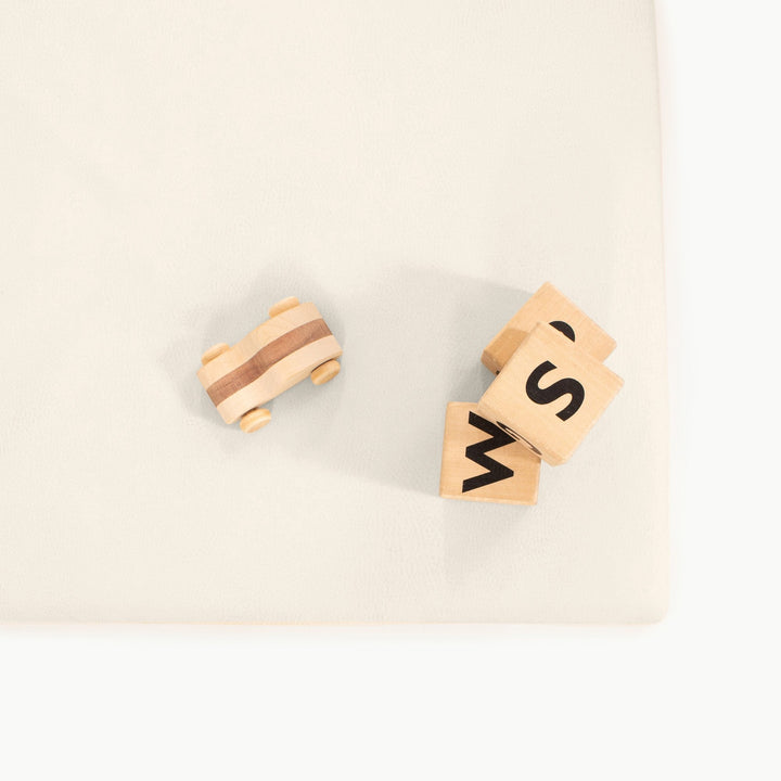 Wooden toy car and alphabet blocks on the ivory vegan leather padded play mat